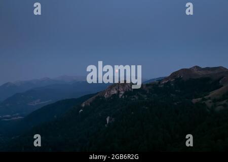 Splendide pleine lune rouge s'élève au-dessus des crêtes de montagne des Apennines. Banque D'Images