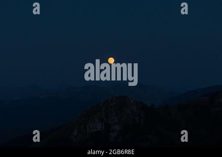 Splendide pleine lune rouge s'élève au-dessus des crêtes de montagne des Apennines. Banque D'Images