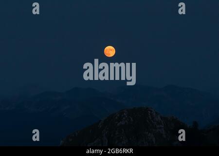 Splendide pleine lune rouge s'élève au-dessus des crêtes de montagne des Apennines. Banque D'Images