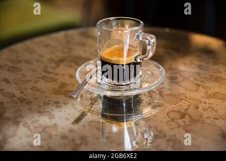 Portrait en gros plan d'une tasse d'espresso en verre de fantaisie, assis sur une table à miroir coloré avec reflet. Banque D'Images