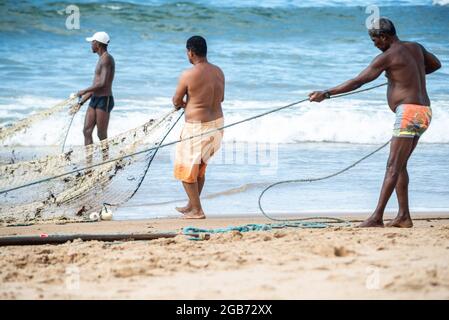 Salvador, Bahia, Brésil - 23 mai 2021 : pêcheurs tirant le filet de pêche de la mer avec des poissons à l'intérieur. Plage de Boca do Rio à Salvador. Banque D'Images