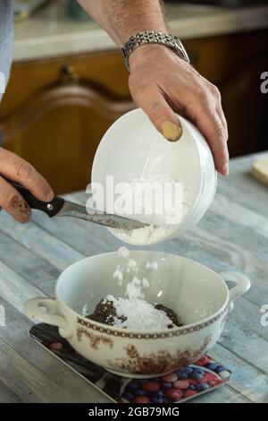 Processus étape par étape de fabrication de chocolats à partir de chocolat noir et de cerises au cognac à la maison. Le sucre en poudre est ajouté à un contenant de cacao râpé Banque D'Images