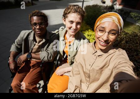 Selfie de jeune femme arabe souriante dans le hijab photographiant avec des amis, y compris un homme aux jambes paralysées Banque D'Images