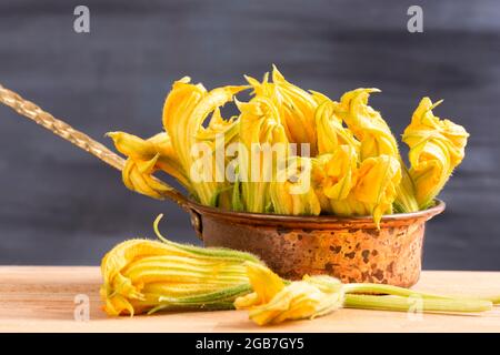 Concept de fleurs de courgettes comestibles crues : fleurs de potiron jaunes fraîches et biologiques en pot de cuivre. Ingrédient sain de style de vie. Cuisine méditerranéenne Banque D'Images