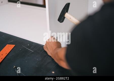 mains clouant une vis avec un marteau dans un morceau de mobilier en bois blanc Banque D'Images