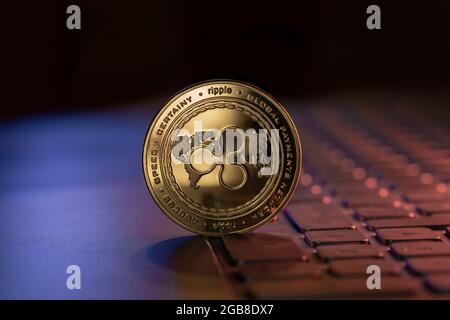 La pièce de monnaie physique crypto-monnaie XRP Ripple est placée sur le clavier de l'ordinateur portable et est éclairée par des lumières bleues et violettes Banque D'Images