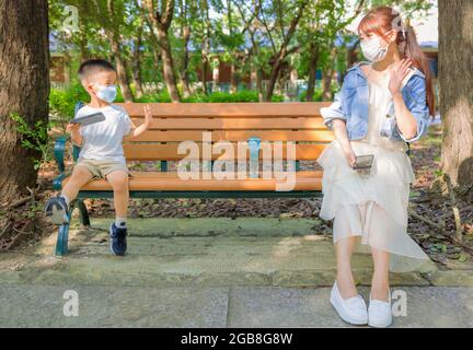 Mère et fils en social distanciation assis sur le banc dans le parc Banque D'Images