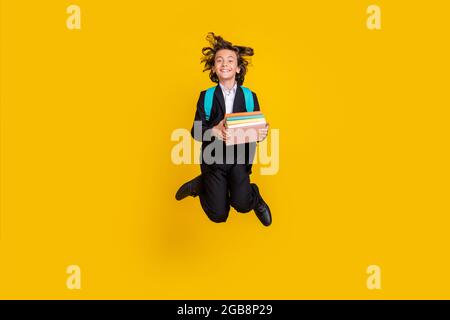 Photo d'un élève scolaire tenir pile livre saut sac de vêtements noir uniforme isolé jaune fond Banque D'Images