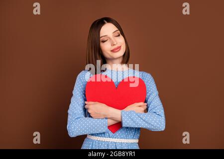 Photo de mignon bob hairdo jeune femme câlin coeur porter chemisier bleu isolé sur fond brun de couleur Banque D'Images