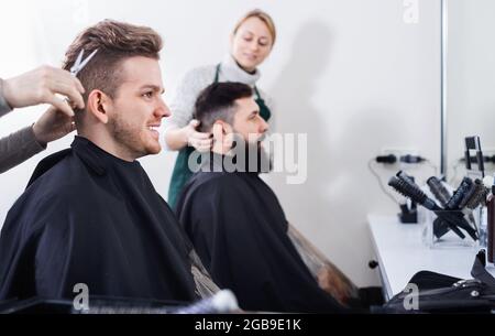 Jeunes clients ayant leurs cheveux coupés par les coiffeurs Banque D'Images