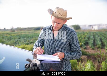 Homme signant des documents près de la voiture de la ferme Banque D'Images