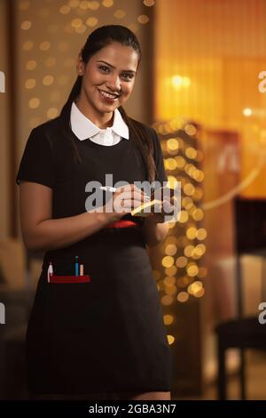 UNE BONNE SERVEUSE REGARDANT L'APPAREIL PHOTO TOUT EN PRENANT DES COMMANDES Banque D'Images