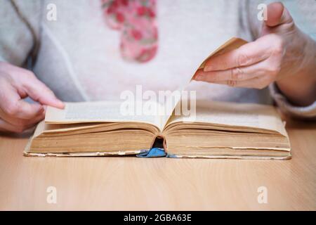 Une femme assise à une table lit et retourne à travers un livre. Mise au point sélective Banque D'Images