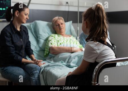 Accent sélectif sur les jeunes petits-enfants qui visitent une grand-mère à la retraite malade dans une salle d'hôpital soutenant pendant un traitement médical. Femme âgée sénior couché dans le lit se rétablissant après une chirurgie médicale Banque D'Images