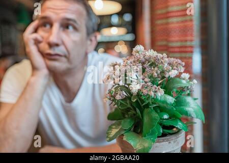 homme en état de dépression avec des émotions tristes sur son visage en attendant dans le restaurant avec une fleur flétristée dans le pot de fleurs Banque D'Images