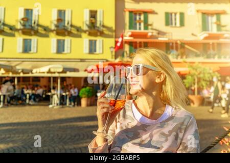 Femme touriste buvant un cocktail au bord du lac corniche dans un pub ouvert de la ville historique d'Ascona en Suisse, dans le canton du Tessin sur le lac Langensee. Banque D'Images