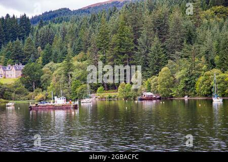 Mystérieux Loch Ness avec des eaux sombres et des rives pittoresques bordées d'arbres, de forêts écossaises et de bateaux Banque D'Images