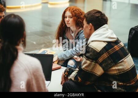 Les étudiants assis dans le hall de l'université ont une discussion. Des adolescents qui font des études de projet ensemble à l'université. Banque D'Images