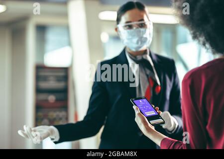 Une femme tenant un smartphone avec une carte d'embarquement au comptoir d'enregistrement de l'aéroport. Une femme s'est présente à l'aéroport en utilisant une carte d'embarquement numérique Banque D'Images