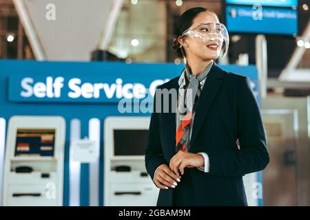 Femme au sol avec un écran facial à l'aéroport pendant une pandémie. Une représentante informative féminine de l'aéroport se tient devant un canal libre-service Banque D'Images