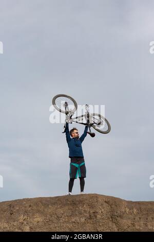 Cycliste barbu sur la montagne tient son vélo dans ses bras au-dessus de sa tête