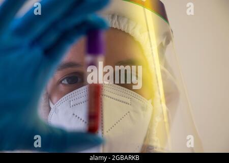 Un médecin avec écran facial tenant une bouteille d'échantillon de sang. Banque D'Images