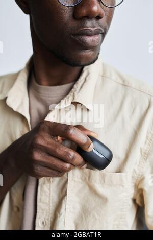 Un jeune homme africain en lunettes de vue en mettant l'étui avec un casque sans fil dans sa poche Banque D'Images