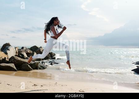 Belle tenue jeune femme courir sur une plage de sable au bord de la mer Banque D'Images
