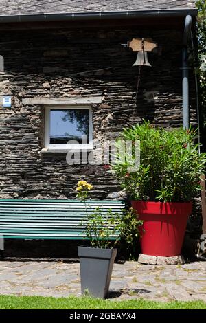 Le coin d'une maison typique en Bretagne en France, en pierres d'ardoise, schiste bleu.Un banc vert est sous une petite fenêtre, un grand pot rouge avec une la Banque D'Images