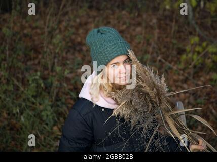 portrait d'une jeune fille belle dans un chaud bonnet tricoté et une veste. et un bouquet de roseaux doux et sec. Marche à l'extérieur, profiter de la nature Banque D'Images