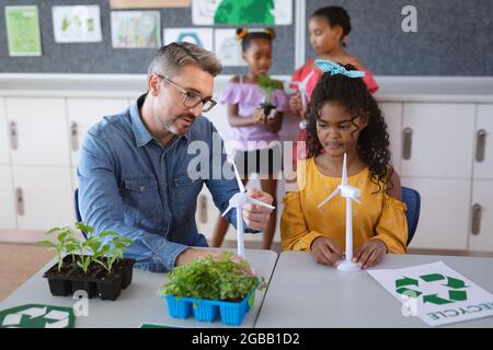 Homme de race blanche enseignant tenant un modèle de moulin à vent enseignant une fille pendant la classe d'environnement à l'école Banque D'Images