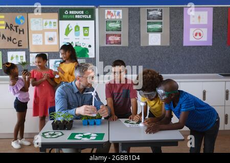 Un enseignant de race blanche tenant un groupe d'enseignement modèle de moulin à vent de divers garçons dans la classe de l'environnement Banque D'Images