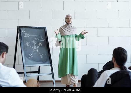 Jeune femme enceinte dans le hijab debout par le tableau noir devant le public Banque D'Images