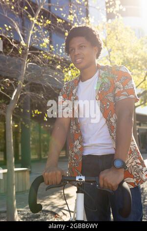 Homme afro-américain en ville souriant et tenant son vélo Banque D'Images