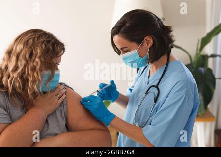 Femme caucasienne médecin portant un masque facial vaccinant la patiente à la maison Banque D'Images