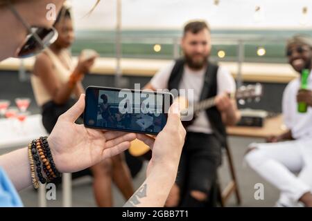 Jeune homme avec un smartphone qui photographie ses amis lors d'une fête sur le toit Banque D'Images