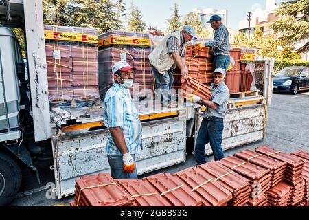 Ankara, Turquie - juillet 2021: Les ouvriers de la construction portant des masques protecteurs déchargent un camion plein de tuiles de toit. Banque D'Images