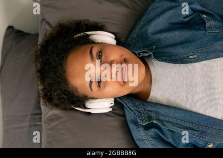 Une jeune fille adorable vous regarde tout en écoutant de la musique de relaxation dans un casque Banque D'Images