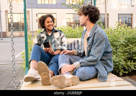 Couple adolescent insouciant en vêtements décontractés assis sur des balançoires et d'interaction Banque D'Images