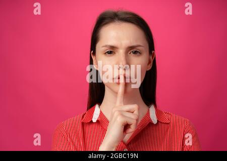 Portrait de la femme tenant le doigt sur les lèvres pour être silencieuse sur fond rose Banque D'Images