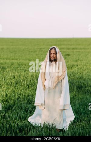 Jésus Christ debout dans la prairie vêtu de sa robe blanche traditionnelle sur fond de ciel. Banque D'Images