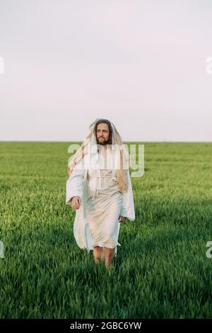 Jésus Christ marchant dans la prairie vêtu de sa robe blanche traditionnelle sur fond de ciel. Banque D'Images