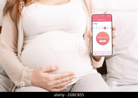 Femme enceinte méconnue montrant une application mobile pour la grossesse Banque D'Images