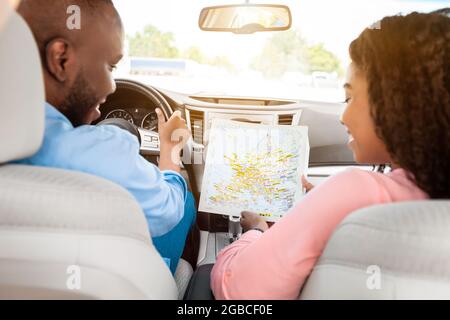 Heureux couple noir regardant la carte papier assis à l'intérieur de la voiture Banque D'Images