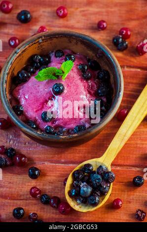 Crème glacée maison aux fruits et aux baies dans un bol sur une table, au milieu des raisins de Corinthe, des canneberges et des bleuets Banque D'Images