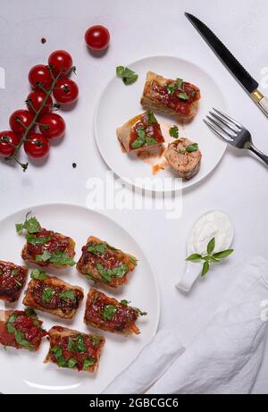 Déposer avec deux assiettes blanches avec des petits pains au chou sauce tomate, des tomates cerises, de la crème sure, de la fourchette et du couteau et de la serviette en lin. Un rouleau est coupé. Blanc Banque D'Images