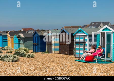 Angleterre, Hampshire, Hayling Island, deux femmes assises devant des cabanes de plage colorées Banque D'Images