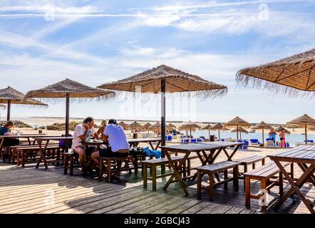 Les gens, les gens qui boivent, les gens qui mangent, les gens assis prenant un verre sous un parasol dans un café restaurant de la plage Fuseta East Algarve Portugal, Banque D'Images