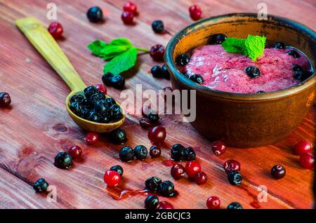 Crème glacée maison aux fruits et aux baies dans un bol sur une table, au milieu des raisins de Corinthe, des canneberges et des bleuets Banque D'Images