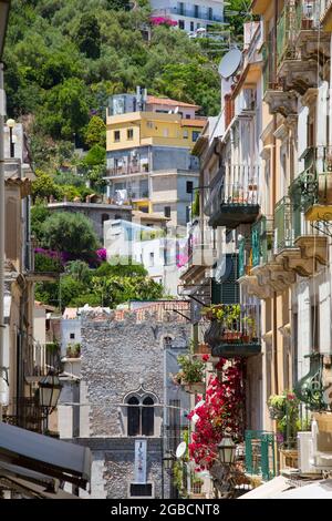 Taormina, Messine, Sicile, Italie. Vue sur la via Teatro Greco à la façade crénelée du Palazzo Corvaja, maisons colorées accrochée à flanc de colline. Banque D'Images